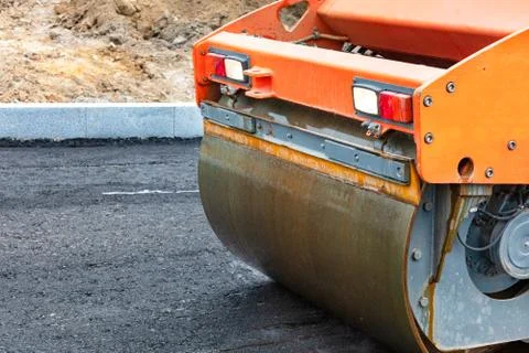 The wheel of a large road vibratory roller compacts fresh asphalt on the new  Stock Photos
