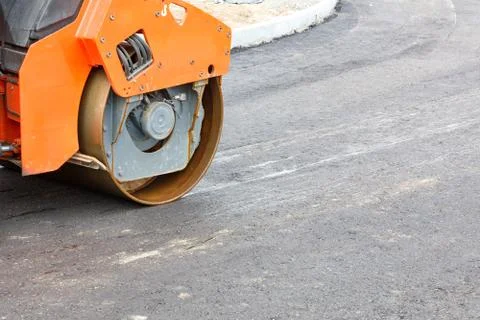 The wheel of a large road vibratory roller compacts fresh asphalt of the new  Stock Photos
