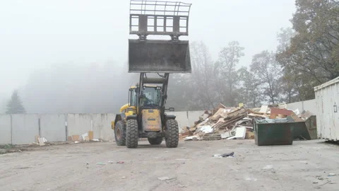 Wheel loader with lifted scrap grapple moving along a recycling center Stock Footage 234208431