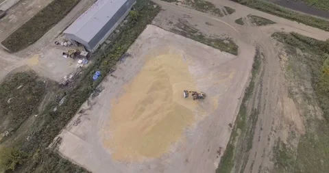 Wheel loader transporting harvested grain pile near warehouse, overhead Stock Footage 296700625