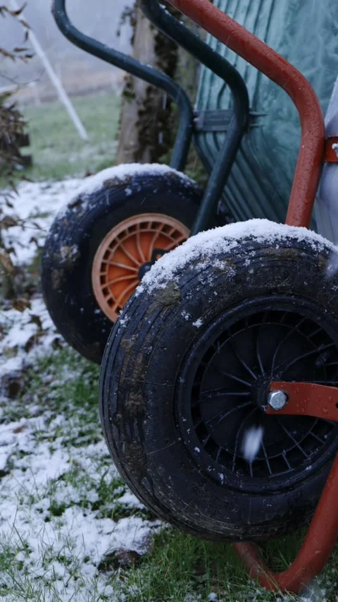 Wheels of two wheelbarrows in a garden are covered by snow during snowfall. Stock Footage 325491162