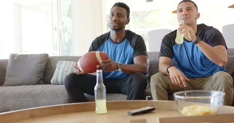 When big play flashes on TV, diverse male friends sipping lemonade and rotating Stock Footage 341943572