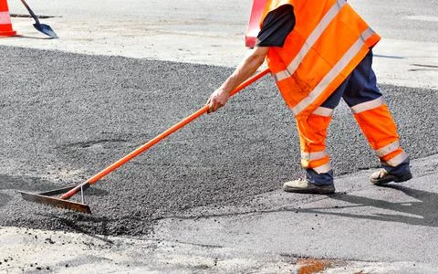 When repairing a road, a worker manually levels the hot asphalt with a metal  Stock Photos