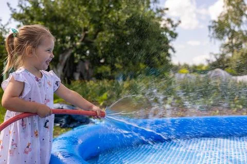 While drawing water into the pool, a happy child closes the hose with his finger Stock Photos