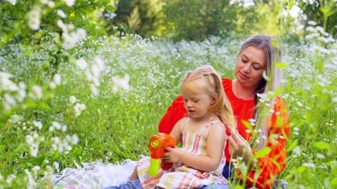 While the girl blows soap bubbles, her mother combs her hair. Video stock 254472499