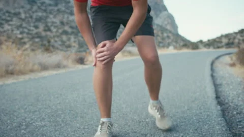 While jogging outdoors, a man experiences sharp pain in his knee, stops running Stock Footage 316680716