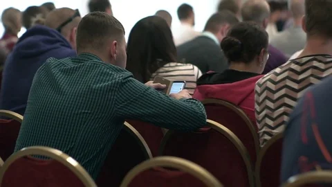 While at the lecture, a young man uses a smartphone. People in the audience Stock Footage 76322555