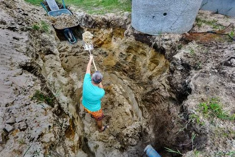 While manually digging pit for septic tank, worker throws soil into garden .. Stock Photos