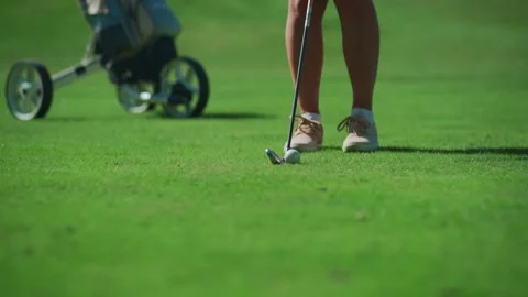 While playing golf, a girl hits the ball with a club and it hits the hole Stock Footage 217956392
