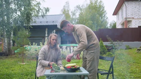 While preparing dinner at the dacha, a man gives a woman vegetables to cut. In Stock Footage 145534000