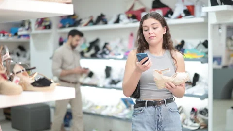 While shopping and choosing shoes, woman scans QR code on sandals product Stock Footage 341532304
