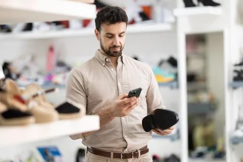 While shopping and choosing shoes, man scans QR code on classic shoes product Fotos de archivo