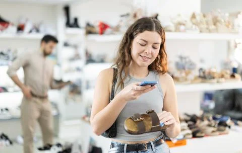 While shopping and choosing shoes, woman scans QR code on sandals product Stock Photos