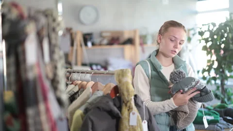 While shopping, girl browsing goods items and choose elect warm hat in store Stock Footage 320451518