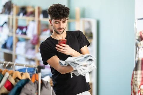 While shopping, guy scans barcode on label of jeans Stock-Fotos