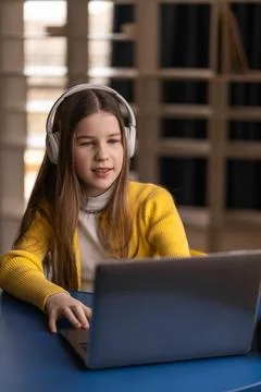 While sitting in a library, a girl studies online with her laptop and headp.. Stock Photos