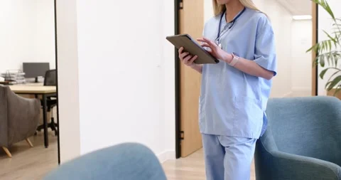 While tapping tablet, healthcare worker is stepping from doorway to blue chair Stock Footage 343838047