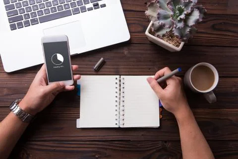 While waiting for installing on smartphone a man write something on notebook  Stock Photos