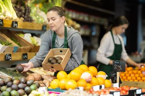 While working in shop, employee forms display case, puts avocado in pile Stock Photos