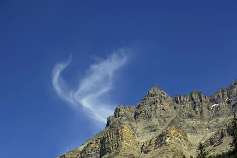 Whimsical Cloud Curl Rises Like Smoke Above a Sharp Rocky Mountain Peak Stock Photos