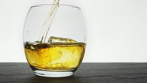 Whiskey being poured over real ice cubes in an oval glass on a dark stone bas Vídeo Stock 123021298