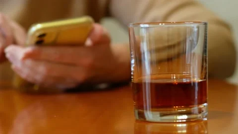 Whiskey glass standing on a table on background of hand with mobile phone, ha 스톡 동영상 170659211