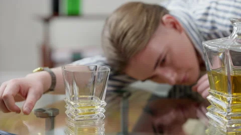 Whiskey in glass on table with blurred face of drunk young man lying at Stock Footage 150487322