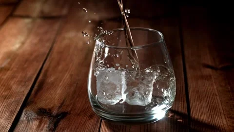 Whiskey on Ice Pouring into a Glass on a Rustic Wooden Table Stock Footage 331102631