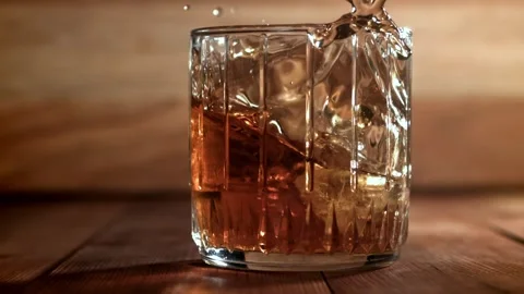 Whiskey on Ice Splashing into a Crystal Glass on a Rustic Wooden Table 库存影片 331102653