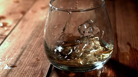 Whiskey on Ice Splashing into a Glass on a Rustic Wooden Table 库存影片 331102206