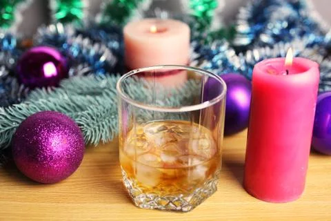 Whiskey or rum with ice on a table with Christmas decorations and burning can Stock Photos