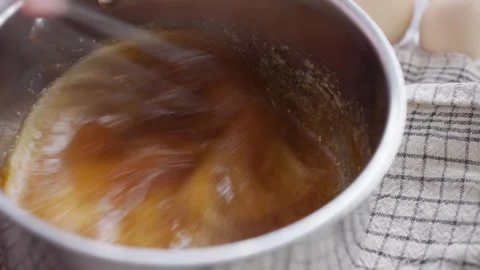 Whisking sweet mixture in a small saucepan, with eggs and kitchen towel nearby Stock Footage 340106361