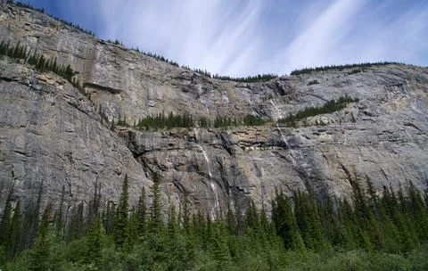 Whispy Cloud Trails Floating Serenely Above Sheer Mountain Stone Cliffs Stock Photos
