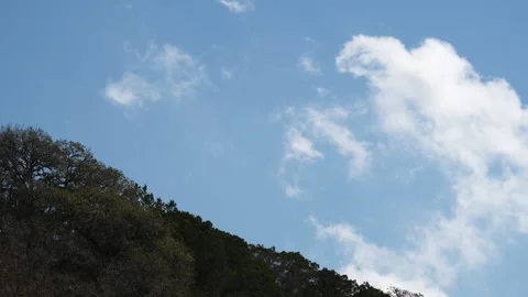 Whispy clouds slowly moving over the tree covered hill tops on a sunny day Video stock 304122961