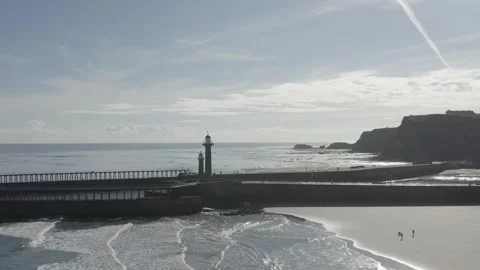 Whitby drone pulling out from lighthouse and pier to reveal beach and tourists Stock Footage 240640843