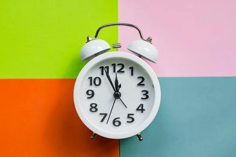 White alarm clock on abstract multicolored paper background. Minimal flat lay Stock Photos