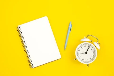 White alarm clock and blank notepad on yellow background, flat lay. Stock Photos