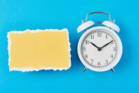 White alarm clock and empty torn paper sheet on a blue background, top view.  스톡 사진