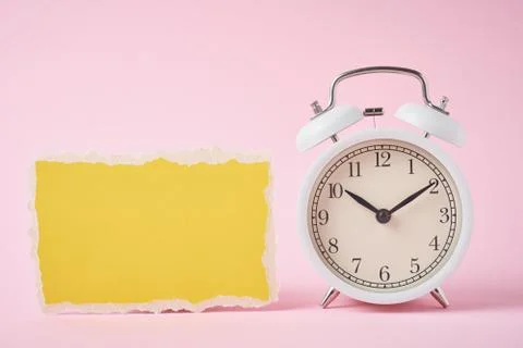 White alarm clock and empty torn paper sheet on a pink background. Time conce 스톡 사진