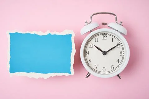 White alarm clock and empty torn paper sheet on a pink background, top view.  写真素材
