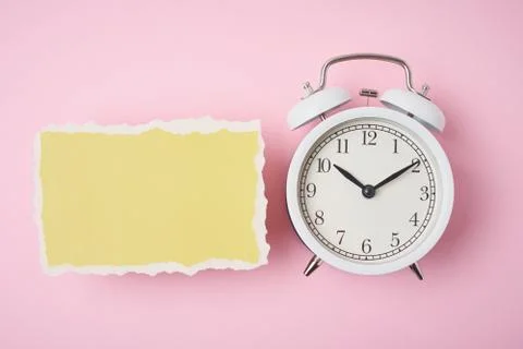 White alarm clock and empty torn paper sheet on a pink background, top view.  스톡 사진