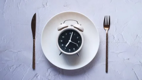 White alarm clock on ceramic plate with gold fork and knife symbolizes inte.. Stock Footage 332777594