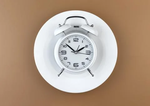 White alarm clock on an empty plate. Intermittent fasting concept. Stock Photos
