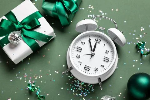 White alarm clock with gift boxes and Christmas balls on green background Stock Photos