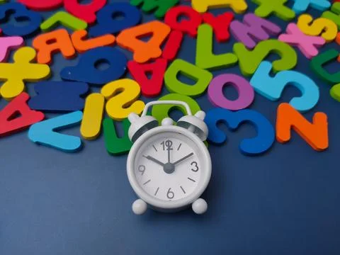 White alarm clock positioned on a blue surface surrounded by scattered colo.. Stock Photos