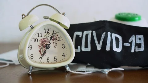 White alarm clock ringing on desk near protective face masks with word COVID-19 Video stock 128554520
