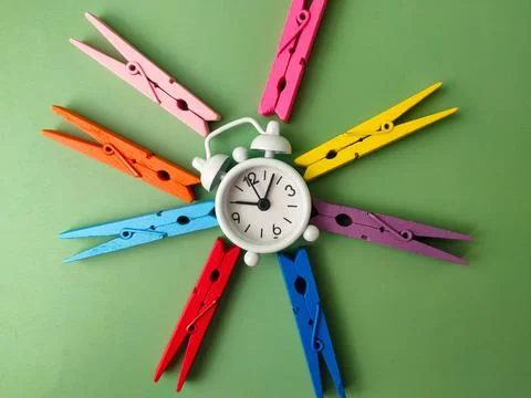White alarm clock surrounded by several colorful wooden clothes pegs on a g.. Stockfoto's