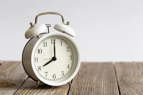 White alarm clock on a wooden surface close-up, blurred white background. Stock Photos
