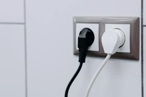 White and black cables in a socket on a white wall. Close up Stock Photos