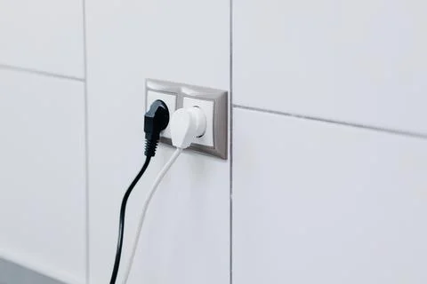 White and black cables in a socket on a white wall Stock Photos